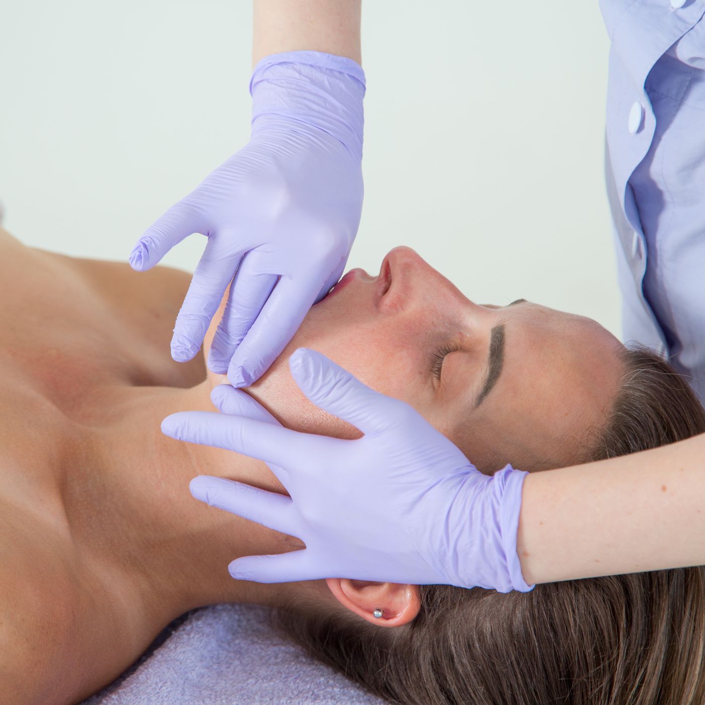 A woman lays on a massage table while recieving a buccal massage from a beauty therapist.