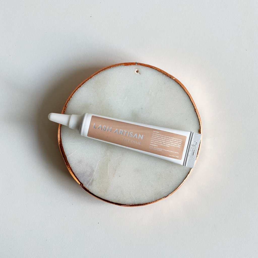 A small tube of lash adhesive from Lash Artisan placed on top of a marble coaster.