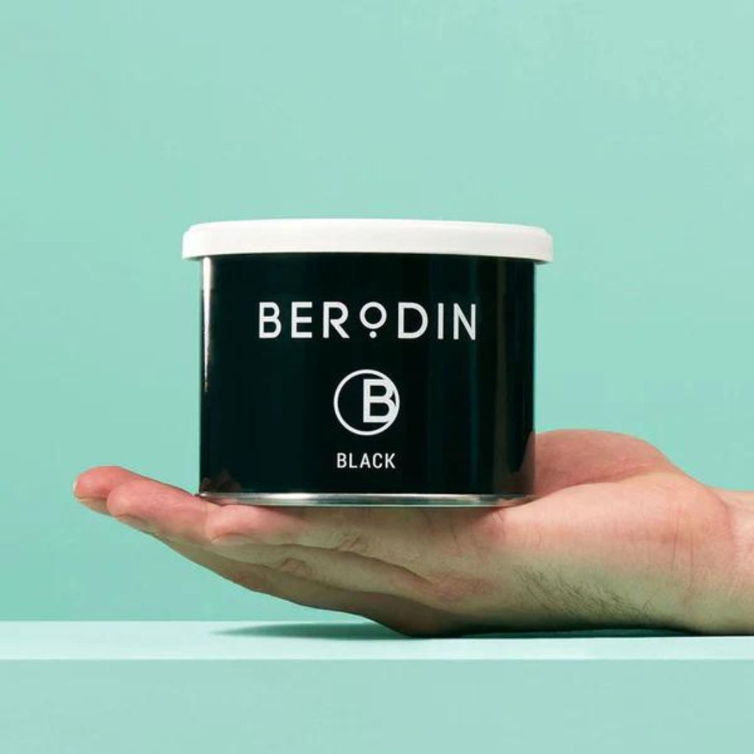 A hand holds a container of Berodin's can of soft black wax.