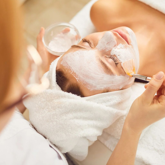 An esthetician uses a brush to apply a cream to their clients face during a spa treatment.