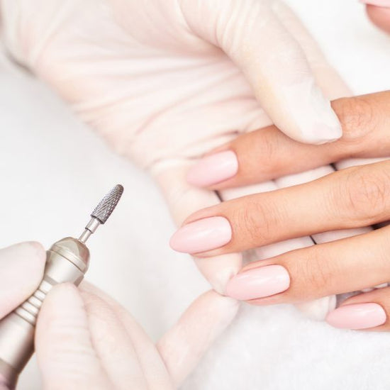 A manicurist wears gloves while holding their client's fingers as they buff their fingernails.