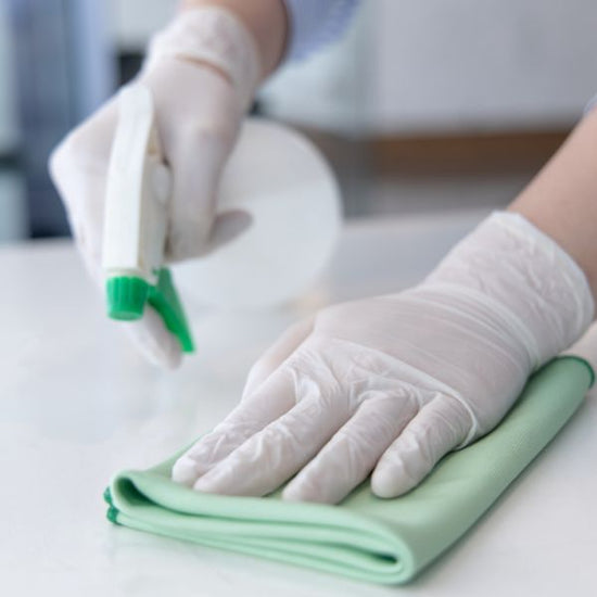 A person wears gloves as they use a spray bottle and cloth to disinfect a counter top.