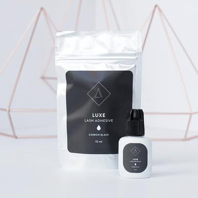 A package of Luxe adhesive and a dropper bottle with a black label on a white background, indicating the product is used for eyelashes.