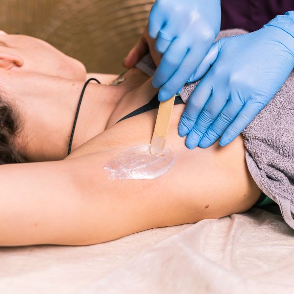 A certified wax technician wears gloved as they apply warm wax to the right armpit of their client.