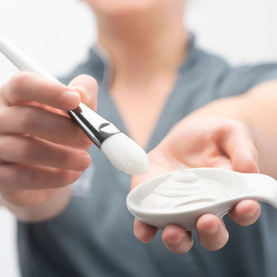 An esthetician shows a facial cream with a brush before she performs a treatment.