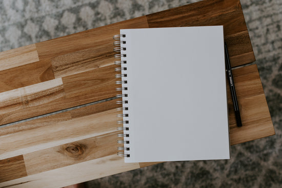 An opened notebook sits beside a pen on a wooden coffee table.